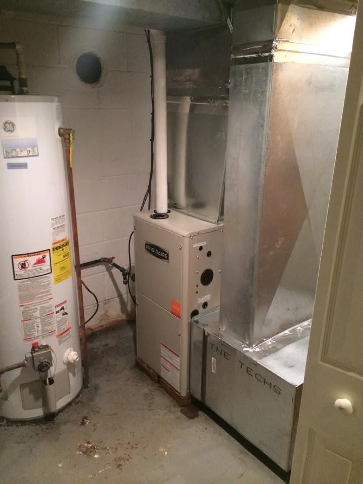 A furnace with new sheet-metal ductwork beside a water heater in a basement