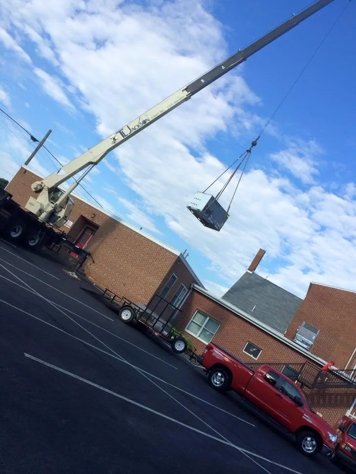 A crane lifting a rooftop unit onto a brick building